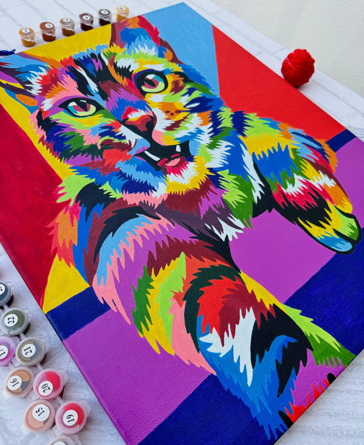 Gato colorido estilo pop art en pintura por números con pincel y pinturas sobre mesa blanca.