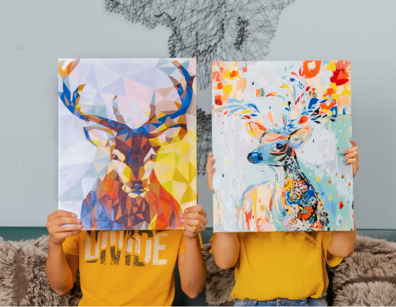 Niños sosteniendo cuadros de renos coloridos para pintar por números, con estilo geométrico y artístico.